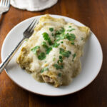 Chicken enchiladas topped with tomatillo sauce and melted cheese on a white plate.