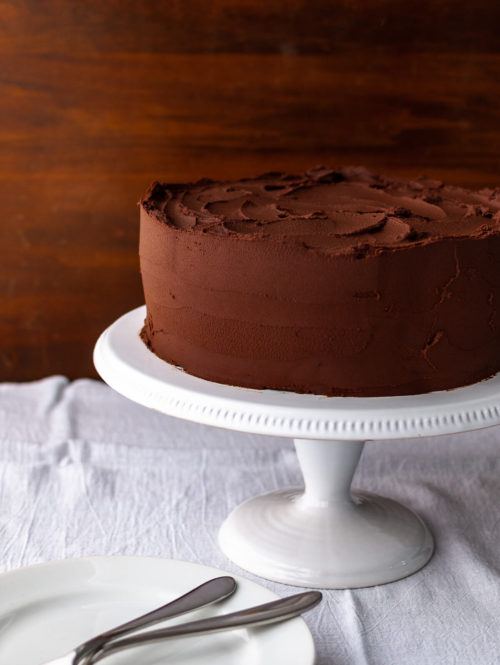 A chocolate cake with chocolate frosting on a white cake stand.