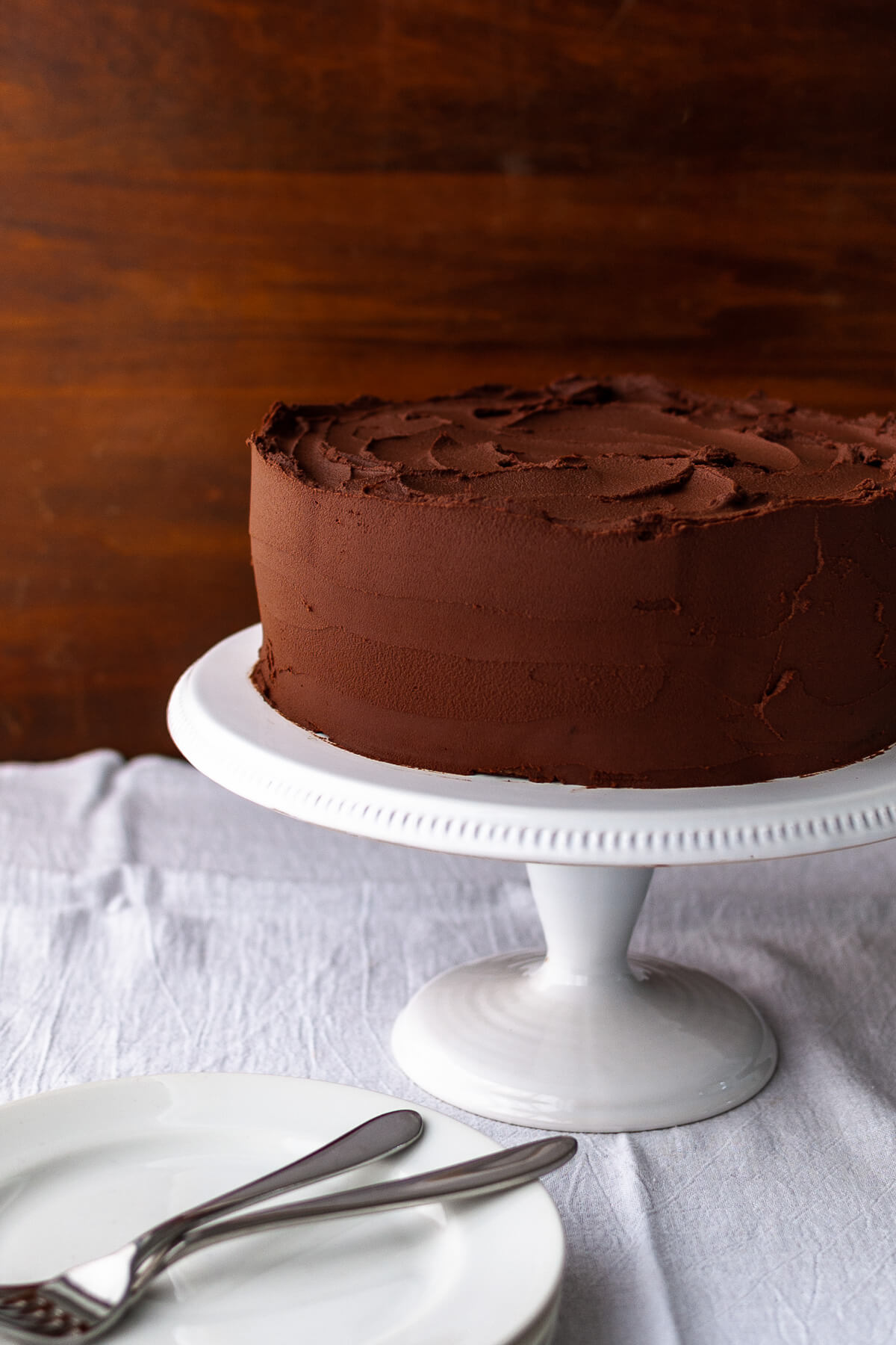 A chocolate cake with chocolate frosting on a white cake stand.
