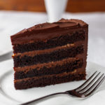 A slice of chocolate cake with caramel filling on a white plate.