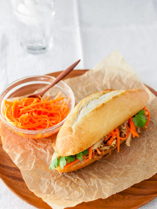 Roasted chicken banh mi sandwich with pickled carrots and cilantro on a wooden plate.