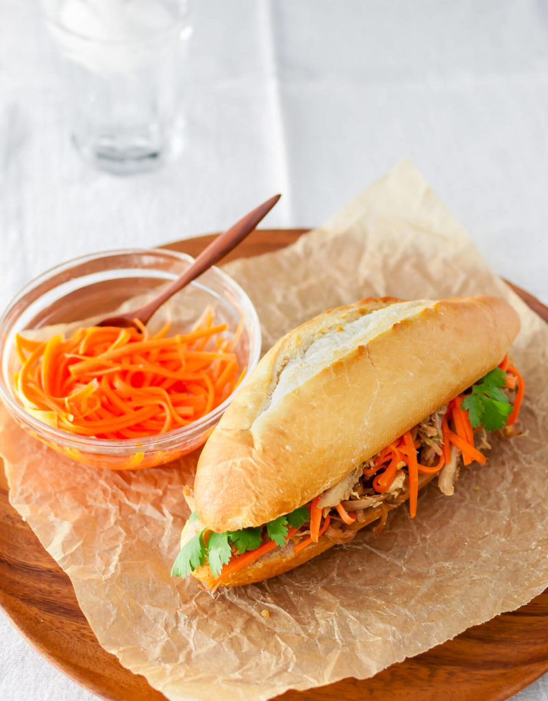 Roasted chicken banh mi sandwich with pickled carrots and cilantro on a wooden plate.
