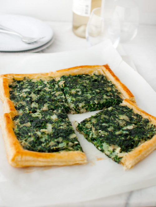 A spinach tart cut into four pieces on a marble board