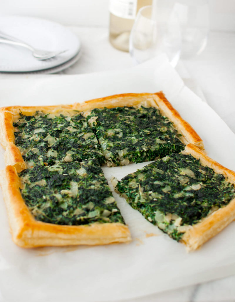 A spinach tart cut into four pieces on a marble board