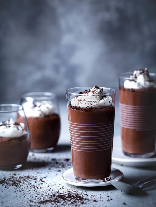 Small glasses of homemade chocolate pudding topped with whipped cream and cookie crumbs.