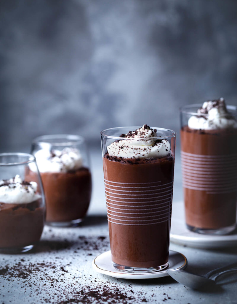 Small glasses of homemade chocolate pudding topped with whipped cream and cookie crumbs.
