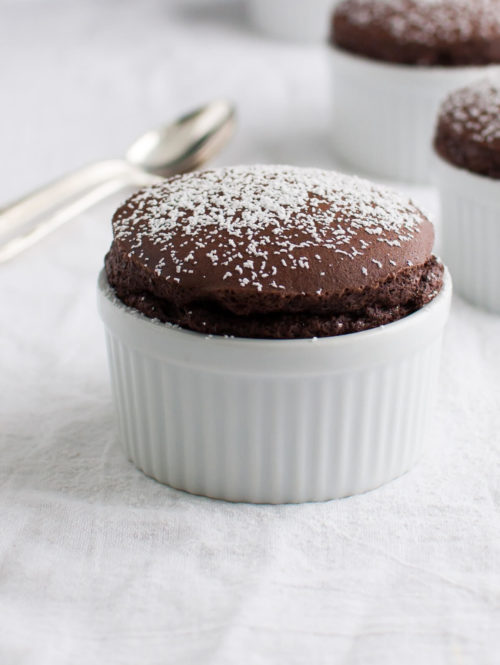 Several chocolate soufflés in small white ramekins sprinkled with powdered sugar.