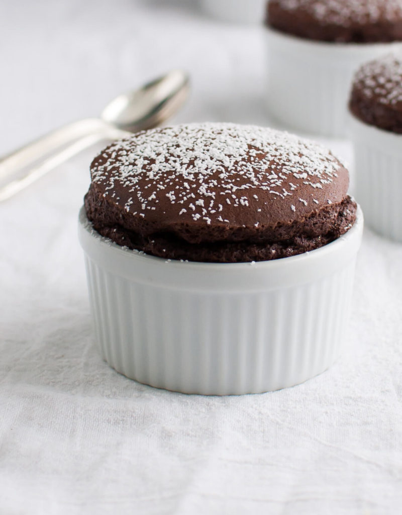 Several chocolate soufflés in small white ramekins sprinkled with powdered sugar.