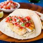 Fish tacos with pico de gallo on a wooden plate.