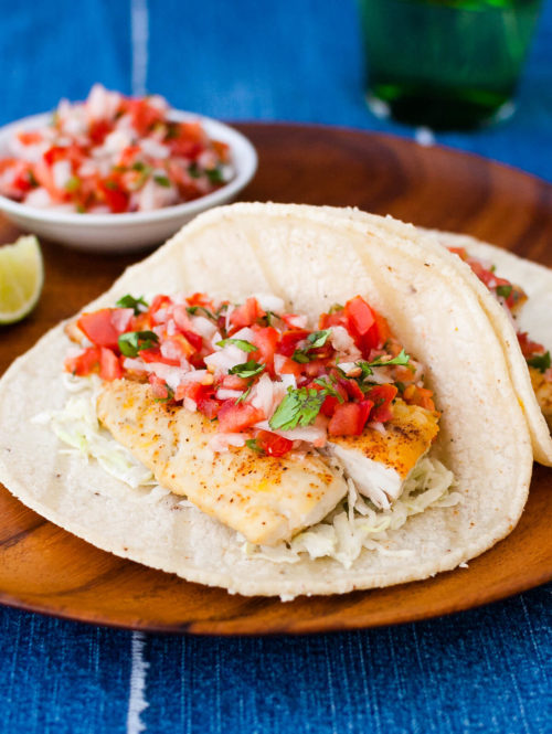 Fish tacos with pico de gallo on a wooden plate.