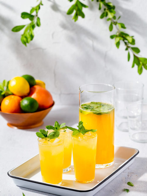 Three glasses and a pitcher of mintade on a white tray.