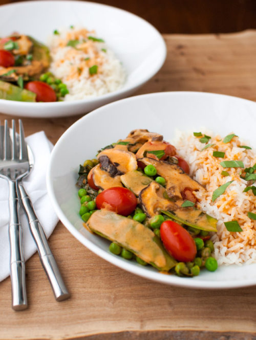 Two plates of vegetable curry with snow peas, mushrooms, and tomatoes served with rice.