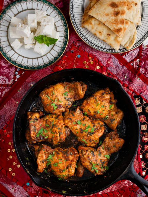 Overhead view of Moroccan chicken in a skillet on a Persian style placemat.