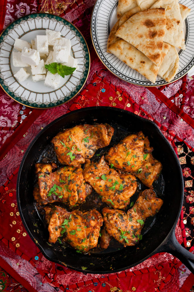 Overhead view of Moroccan chicken in a skillet on a Persian style placemat.