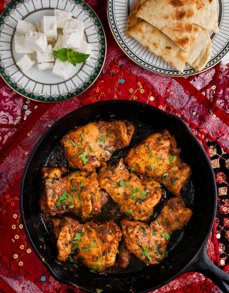 Overhead view of Moroccan chicken in a skillet on a Persian style placemat.