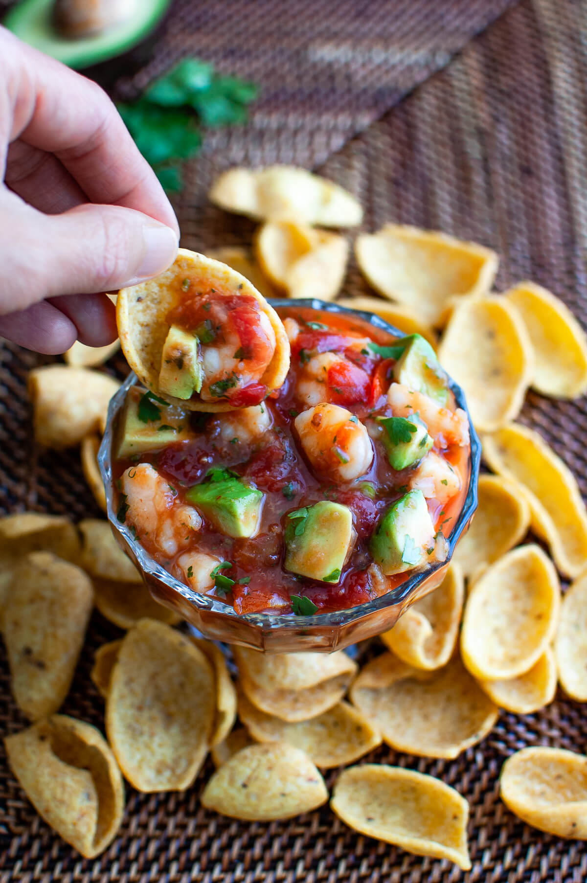 Someone dipping a chip into a bowl of shrimp campechana.