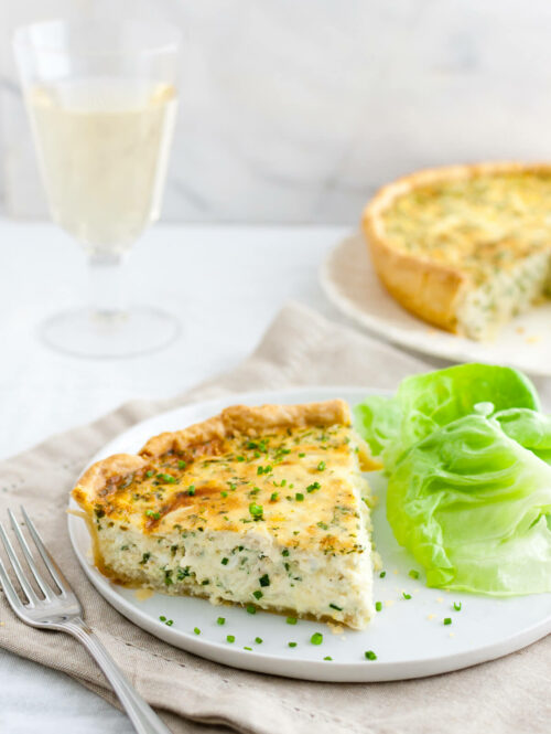 Crab quiche garnished with chopped chives served with a glass of white wine.