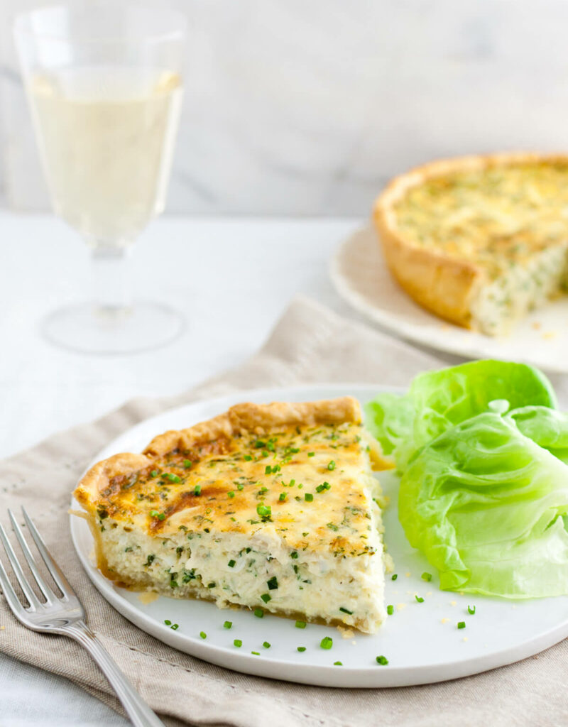 Crab quiche garnished with chopped chives served with a glass of white wine.