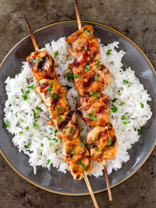 Some grilled chicken skewers on a bed of white rice on a gray plate.