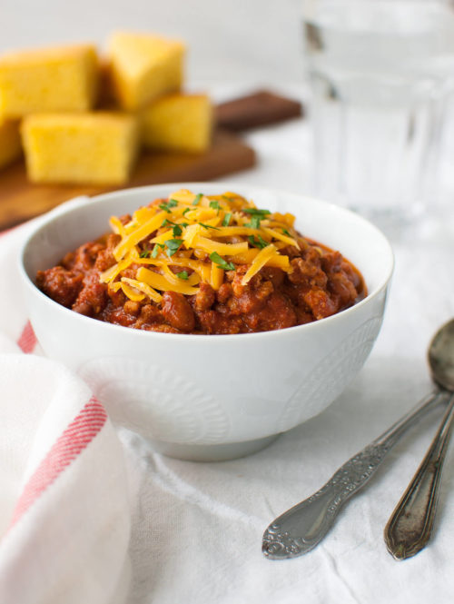 A bowl of chili topped with grated cheddar cheese.