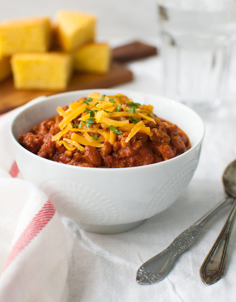 A bowl of chili topped with grated cheddar cheese.