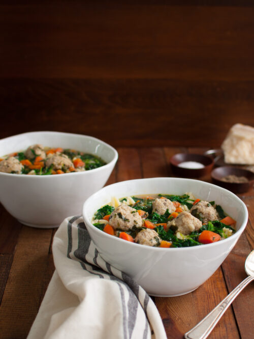 Two bowls of Italian wedding soup on a wooden board.