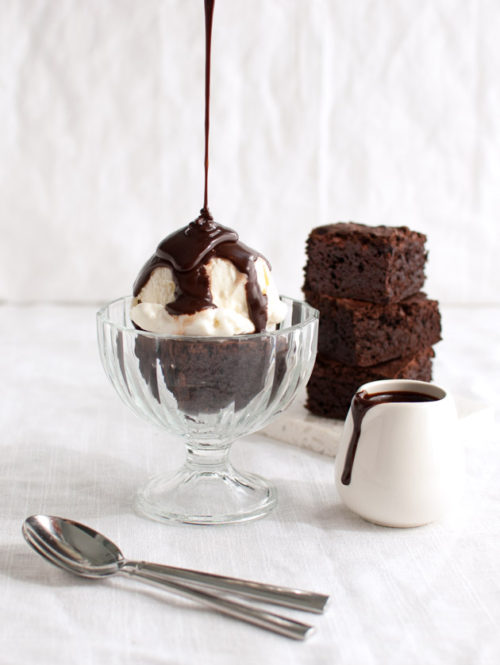 Chocolate sauce being poured on a brownie sundae.
