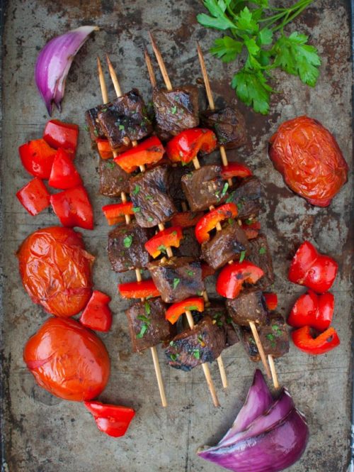 Skewers of beef kebabs next to some grilled tomatoes and onions.