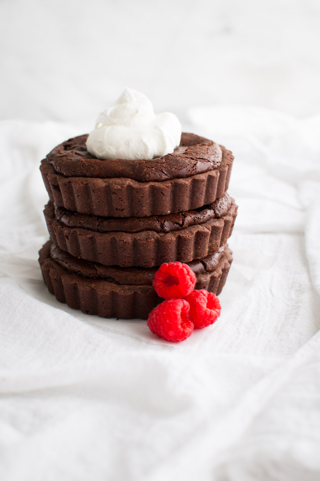 A stack of three chocolate raspberry tartlets garnished with some whipped cream and fresh raspberries.