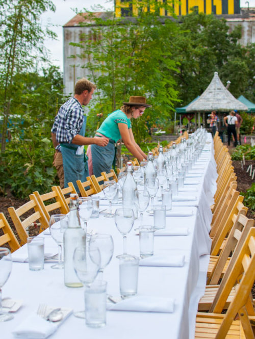 Two setting a long table with wine glasses and napkins