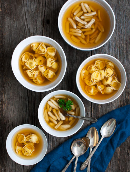 Several bowls of tortellini in brodo on a wooden background.
