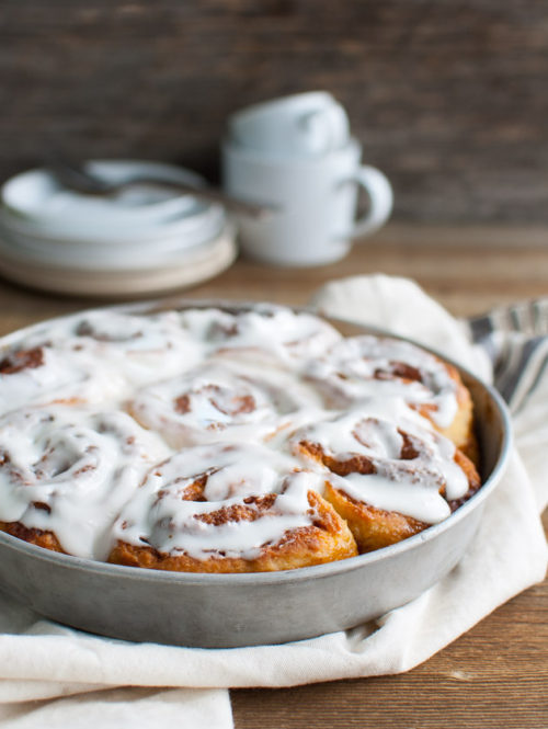 A pan of iced cinnamon rolls on a wooden table top.