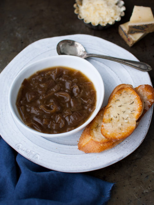 A bowl of French onion soup next to some cheese crostini.