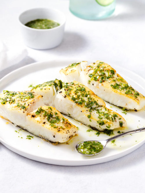 Roasted halibut topped with cilantro-lime sauce on a white plate.