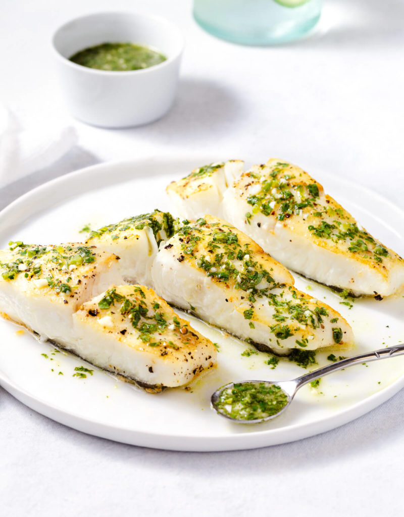 Roasted halibut topped with cilantro-lime sauce on a white plate.