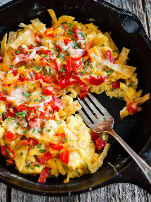 Overhead view of migas topped with chopped tomatoes and melted cheese in a cast iron skillet.
