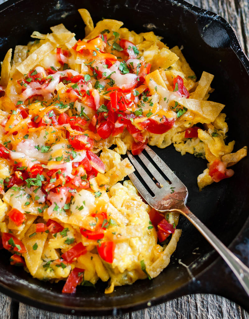 Overhead view of migas topped with chopped tomatoes and melted cheese in a cast iron skillet.