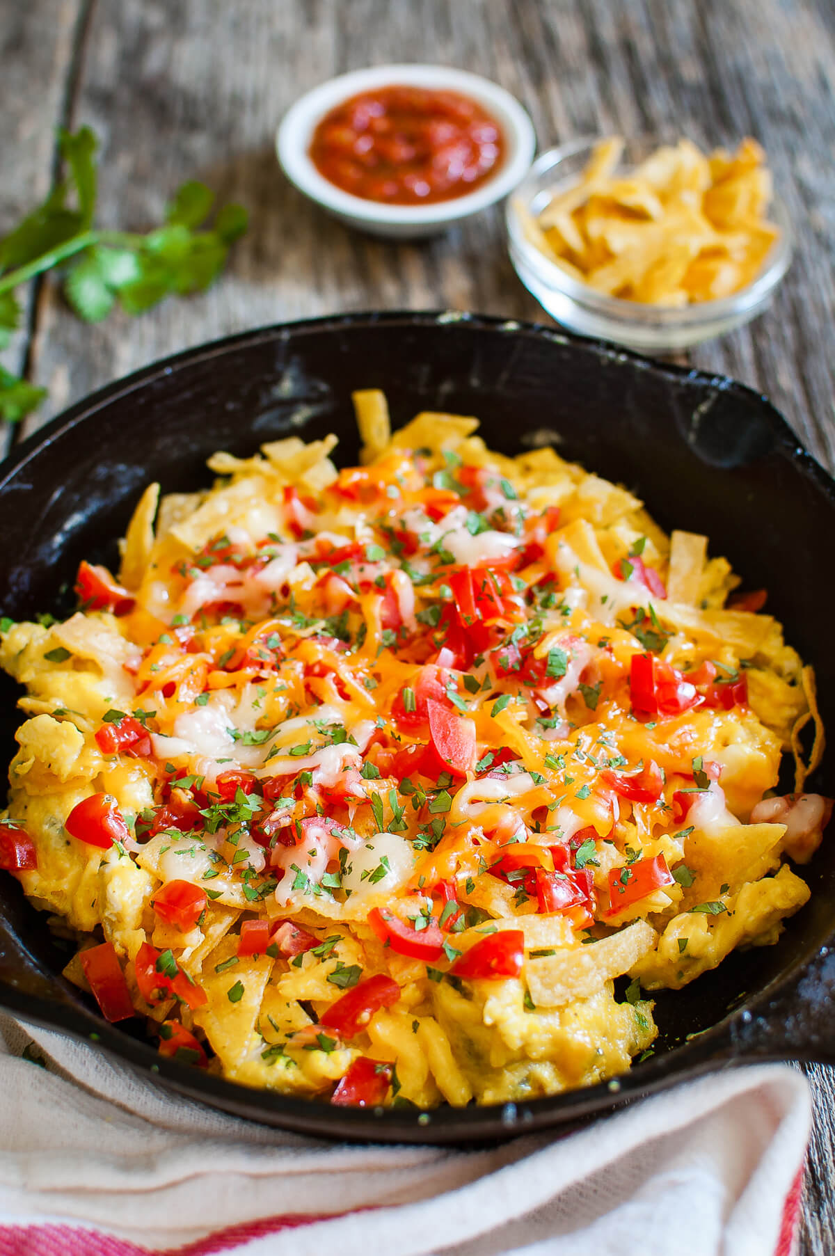 Close-up of migas topped with chopped tomatoes and melted cheese in a cast iron skillet.