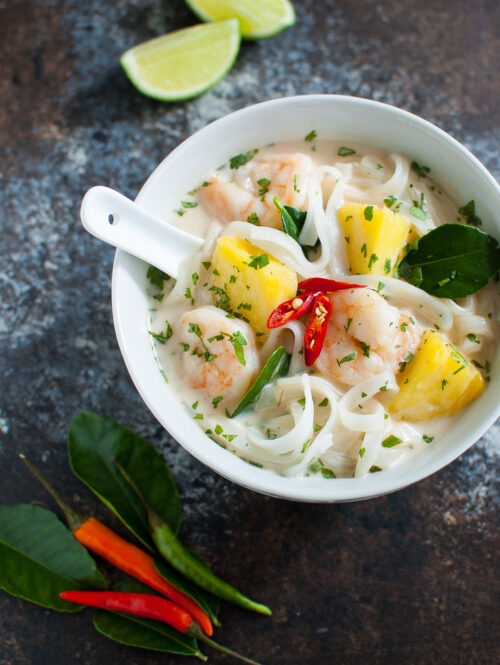 Bowl of Thai coconut soup with shrimp, pineapples, and flat noodles.