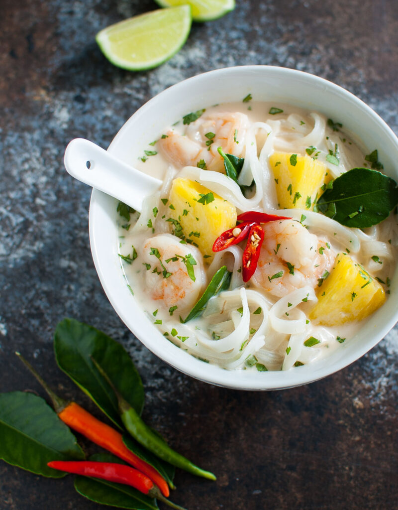 Bowl of Thai coconut soup with shrimp, pineapples, and flat noodles.