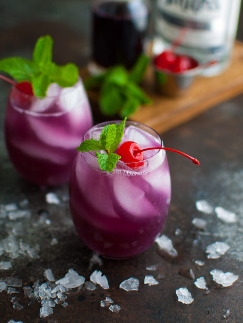 Glass of hibiscus tea cocktail garnished with mint and a maraschino cherry.