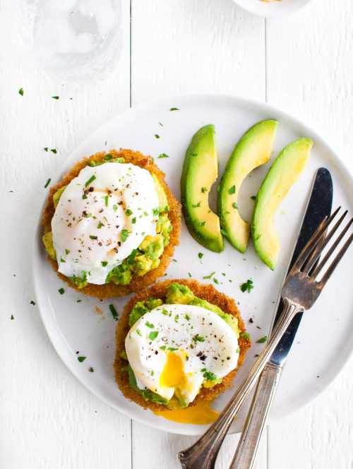 Overhead view of two slices of fried green tomatoes topped with avocado and a poached egg on a white plate.