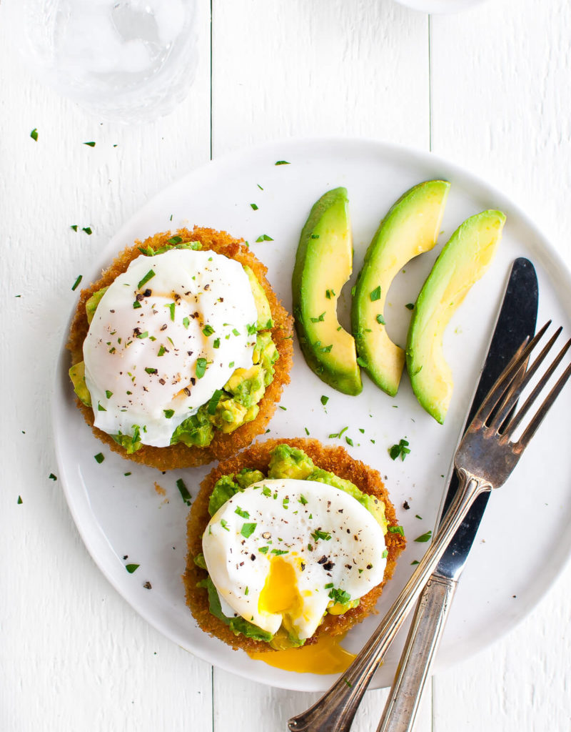 Overhead view of two slices of fried green tomatoes topped with avocado and a poached egg on a white plate.