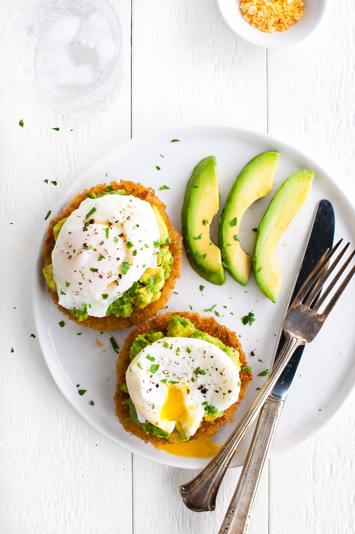 Overhead view of two slices of fried green tomatoes topped with avocado and poached eggs on a white plate.