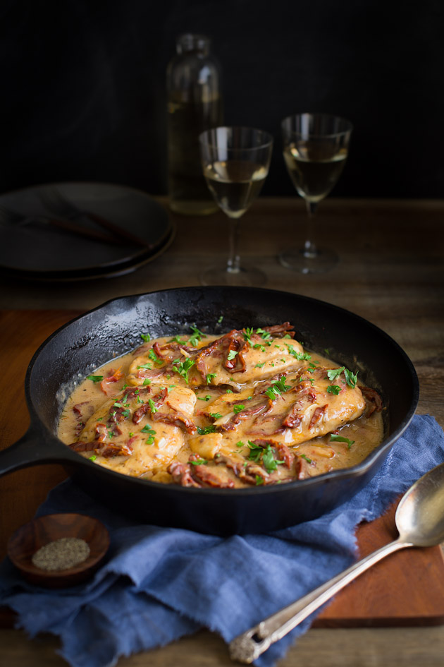 Chicken breasts topped with sun-dried tomatoes in a creamy sauce in a cast iron skillet.