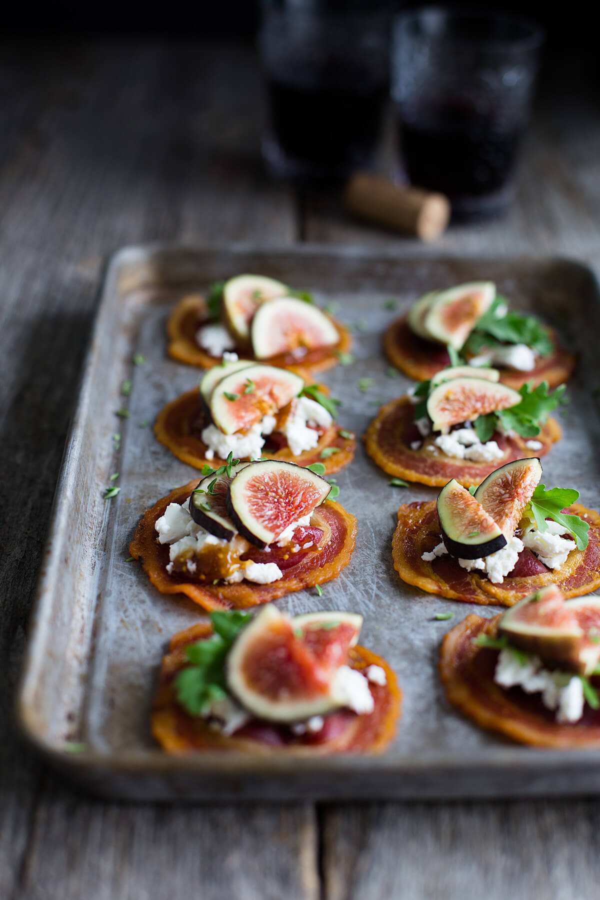 Tray of pancetta crisps topped with goat cheese, figs, and baby arugula.