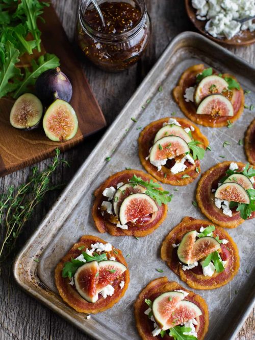 Overhead view of tray of pancetta crisps topped with goat cheese, figs, and baby arugula.