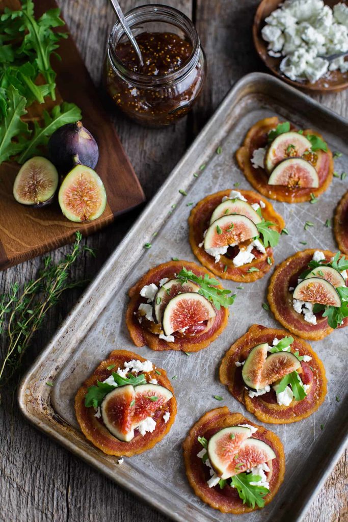 Overhead view of tray of pancetta crisps topped with goat cheese, figs, and baby arugula.