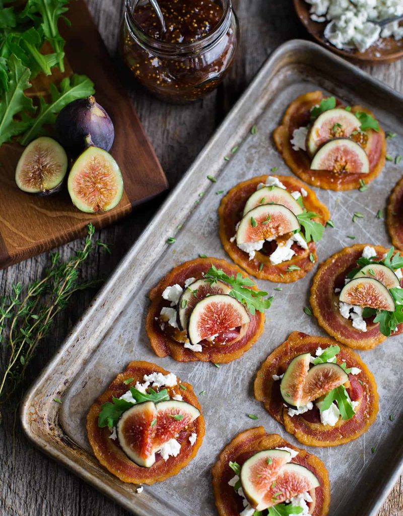 Overhead view of tray of pancetta crisps topped with goat cheese, figs, and baby arugula.