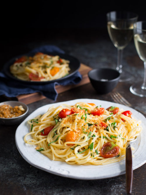 A plate of spaghetti with tomatoes, basil, and bread crumbs.